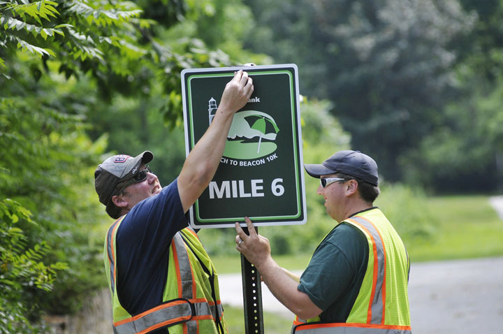 Darren Brown, left, and Jason Emery of the Cape Elizabeth Public Works Department put up the Mile 6 Marker along the Beach to Beacon 10K Road Race course today.