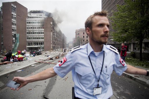 An official attempts to clear away spectators from buildings in the centre of Oslo, Friday July 22, 2010, following an explosion that tore open several buildings including the prime minister's office, shattering windows and covering the street with documents.(AP Photo/Fartein Rudjord) NORWAY OUT: