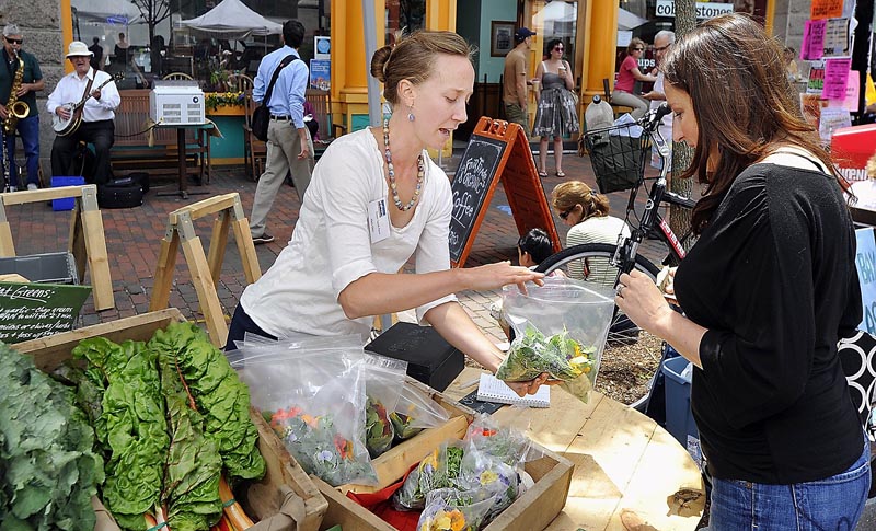 Stephanie Hedlund, owner of Clara Burke Kitchen, shops for local produce at the Monument Square Farmers Market. Here she buys fresh greens and edible flowers from Mary Ellen Chad of Green Spark Farm.
