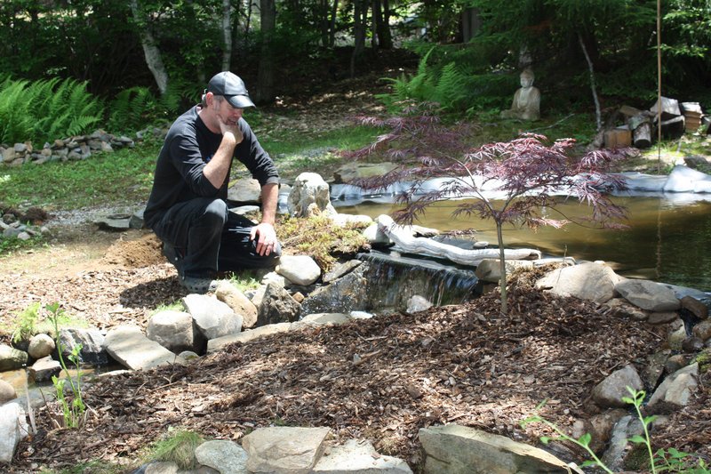 Island Micro Farm owner Mark Shain contemplates the rock placement around the farm's newly expanded water feature.