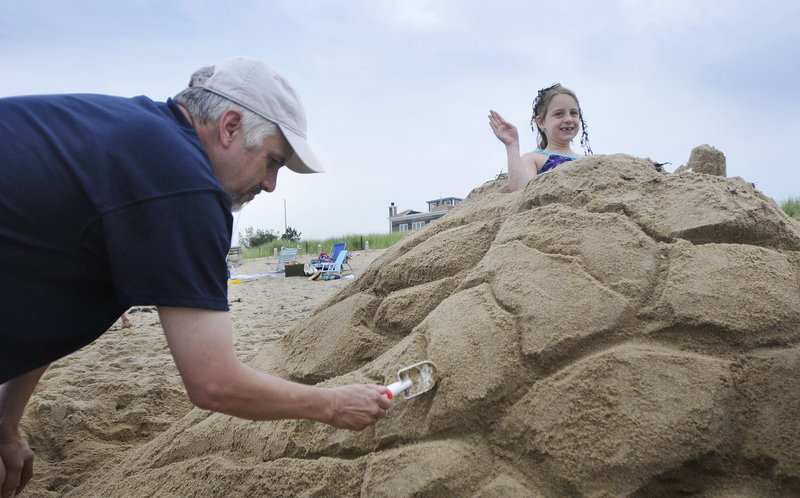 Emma McPartlen, 7, of Worcester, Mass., waves to spectators as her grandfather Bob Bourque of Northborough, Mass., sculpts the form of a mermaid around her at Ocean Park.