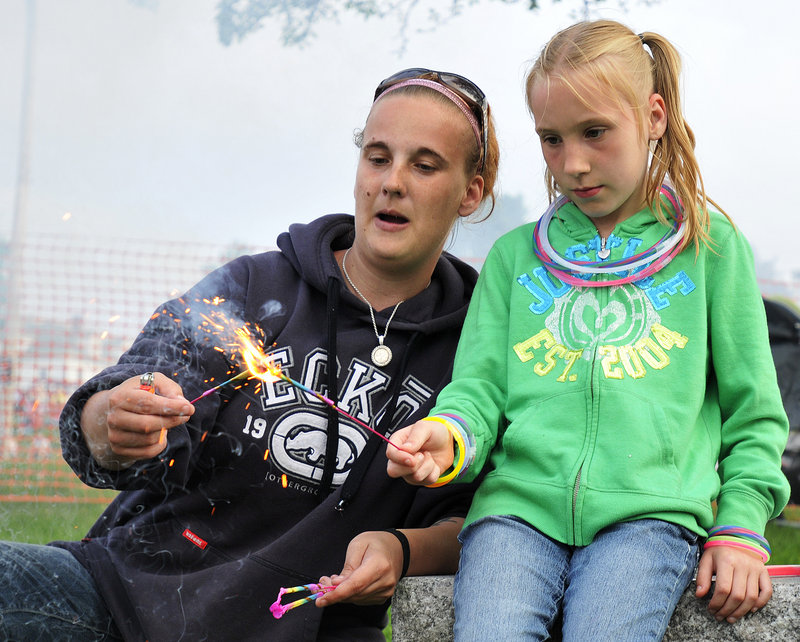 Amanda Nelson helps her 9-year-old daughter, Liticia, light a sparkler at the Eastern Promenade.