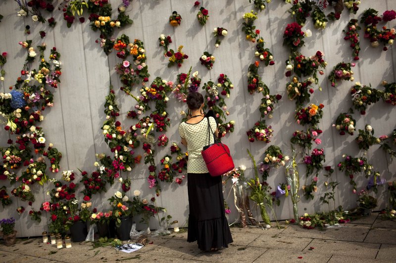 A woman pays respects at a wall decorated with flowers in memory of the victims of Friday’s bomb attack and shooting rampage in Oslo, Norway, on Tuesday.