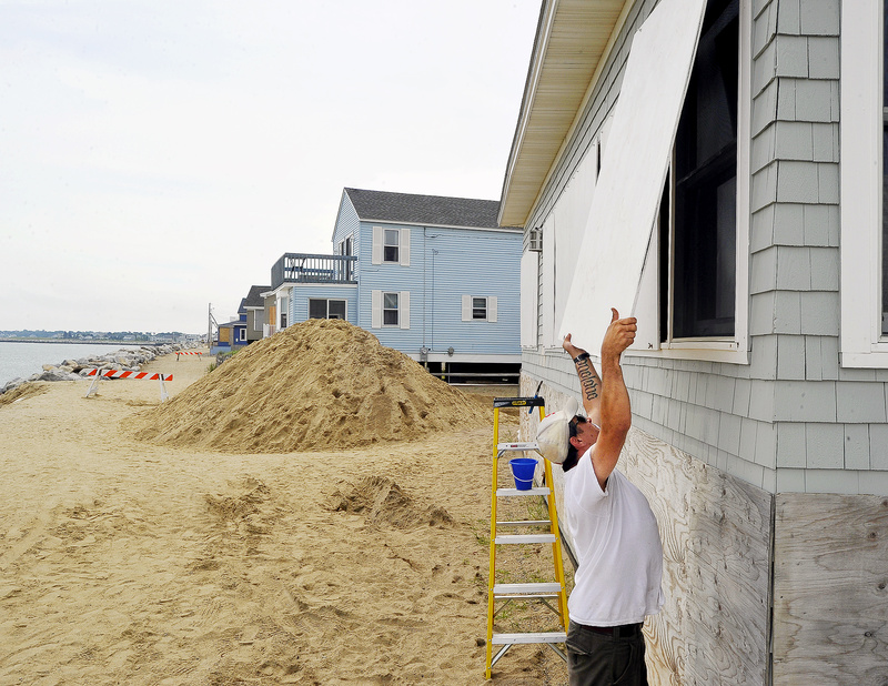 Joe Harvey, owner of Harvest Homes Property Management Co. in Portland, installs plywood window protectors on a client’s house on Surf Street in Camp Ellis on Saturday in preparation for Irene. The pile of sand was dumped in front of the street to help prevent flooding. Along the Eastern Seaboard, cities shut down transportation systems and ordered evacuations.