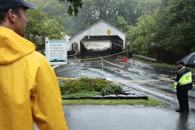 Emergency crews keep people at a safe distance as water from the Ottauquechee River overcomes the Quechee Covered Bridge yesterday. Rising water caused evacuations from the apartment buildings along the Green, flooded the interior of Simon Pearce and eventually swept the bridge away.