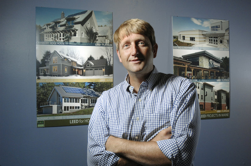 Gunnar Hubbard, an architect who is the founder and CEO of Fore Solutions, a green building consulting firm, stands in front of photographs of a few of the projects his company has worked on in Maine.