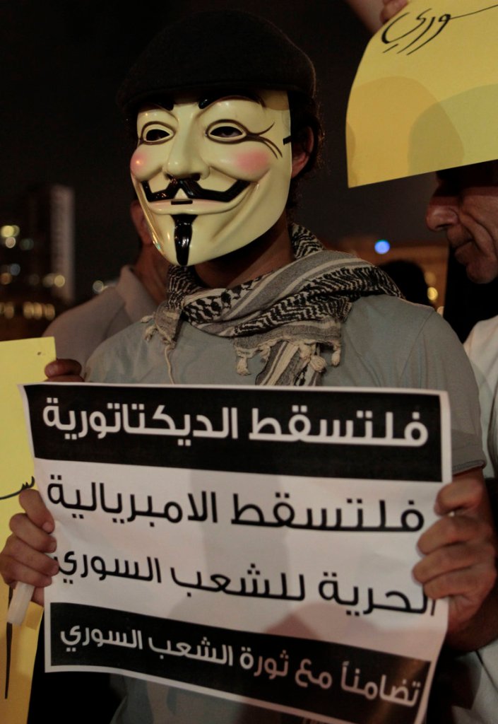 A masked protester holds a placard Monday that reads in part, “Down with dictatorship, freedom for the Syrian people,” during a sit-in by Lebanese intellectuals and journalists.