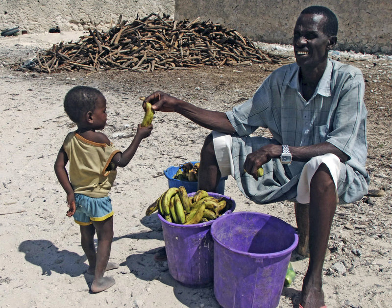 A Somali child receives a banana from a vendor outside a refugee camp in Mogadishu. Refugees say they are often made to return food after they’ve been photographed with it.