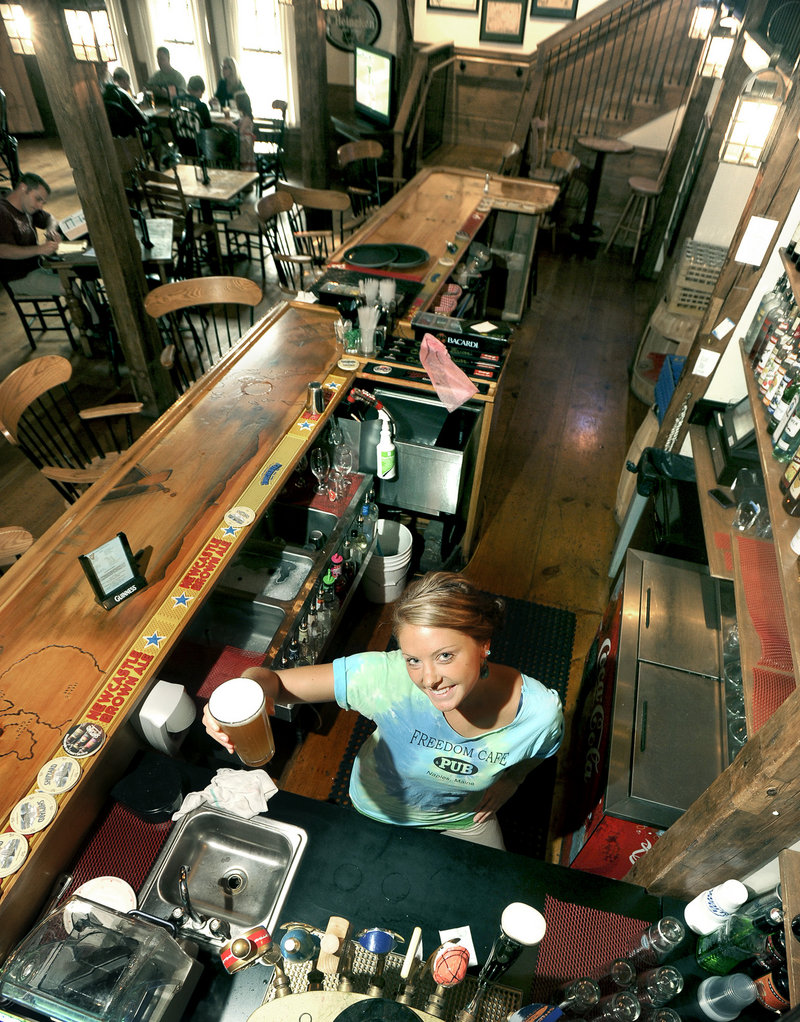 Bartender Annie Foster holds a draft beer at Freedom Cafe and Pub in Naples, located in a 200-year-old converted post-and-beam structure overlooking the edge of Long Lake.