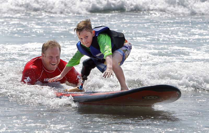 Shaun McLaughlin, a Natick, Mass., 6-year-old who was born without a right foot, learns how to surf with help from Dana Cummings at Long Sands Beach in York on Thursday. Cummings, a Maine native, leads AmpSurf, an organization that teaches people with disabilities how to surf.