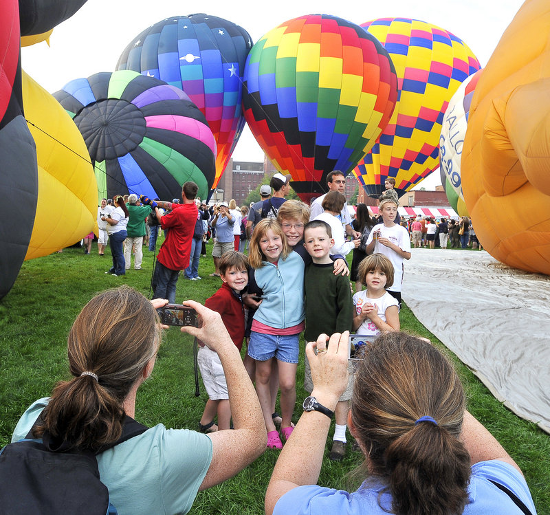 Whitney Condit of Auburn, left, and Elizabeth Townsend, who was visiting from Falls Church, Va., take photos of their families as the hot air balloons are inflated behind them at Railroad Park in Lewiston during the Great Falls Balloon Festival on Saturday.