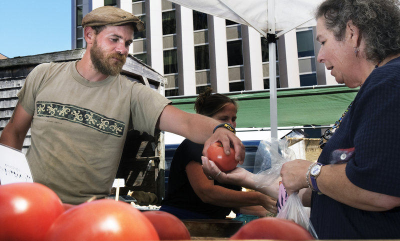 Chris Cavendish of Fishbowl Farms in Bowdoinham hands a tomato to a customer at the farmers market last week.