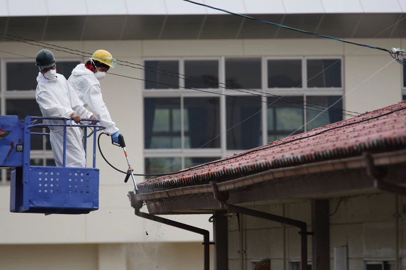Workers decontaminate a gutter around the roof of Yasawa Kindergarten in Minami-Soma, about 12 miles from the tsunami-crippled Fukushima Dai-ichi nuclear facility, earlier this month. Radiation levels are expected to remain high at many sites near the power plant.