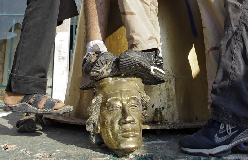 Rebel fighters trample on the head that was broken off a statue of Moammar Gadhafi inside the leader's main compound in Tripoli on Tuesday.
