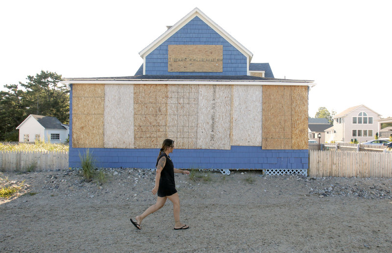 A woman walks past a boarded-up home along Surf Avenue in Saco on Friday. A few houses in the area, which was pounded by a nor’easter on Patriots Day in 2007, were boarded up in preparation for Hurricane Irene.