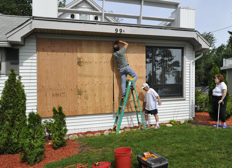 Owner Clare Gambino, right, watches as Larry Skillings, a builder from Cape Elizabeth, left, attaches plywood panels to her home on East Grand Avenue in Scarborough with the help of John Gambino, her husband. It is the first time in 32 years they made the decision to protect their home from a storm, according to the Gambinos.