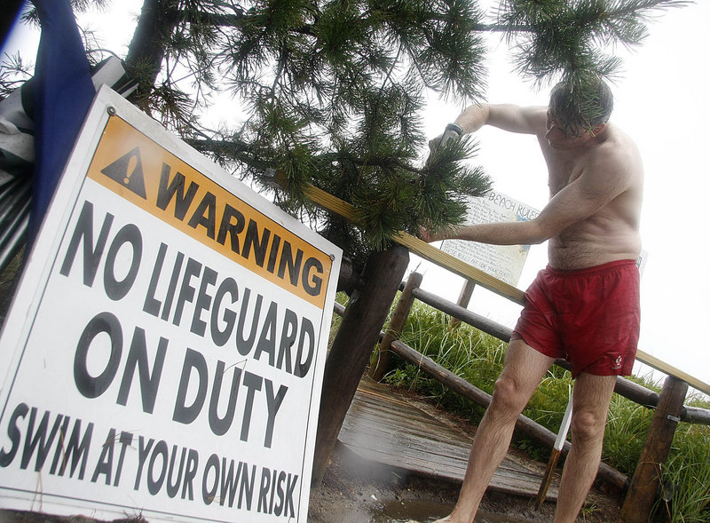 Steve Opre, a lifeguard with the Ferry Beach Park Association, secures a sign alerting visitors that conditions are unsafe for swimming near Surf Street in Saco on Sunday morning. The state's southern coast drew many storm watchers Sunday.