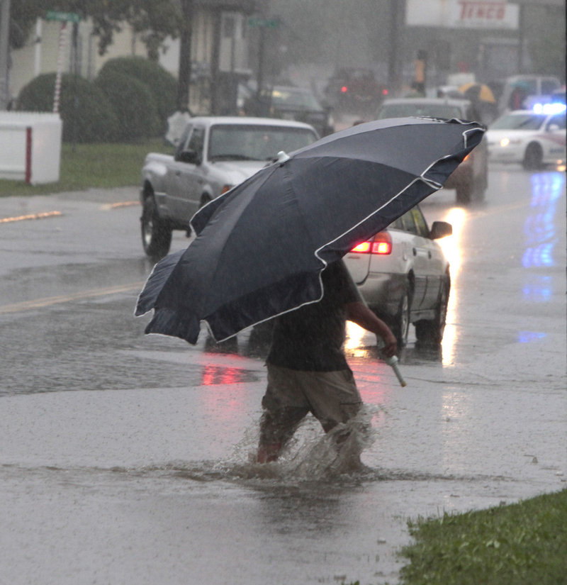 A pedestrian uses a beach umbrella to keep off the rain from Tropical Storm Irene on Sunday in Barre, Vt. Elsewhere in the state, a young woman was missing after she was swept away by the Deerfield River in the southern Vermont town of Wilmington.