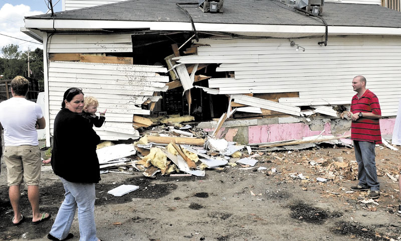 Brenda DiMeo carries a child while she and family members survey the damage to their Cambridge General Store after a loaded pulp truck lost control and crashed into the building around 4 a.m. Tuesday. No one was hurt, but the store on Route 150 sustained extensive damage, and a parked car was destroyed by the rolling logs, said police.