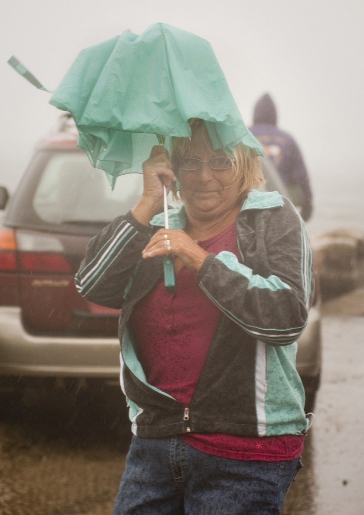 Claire McIntyre of Biddeford tries to stay under cover of a wind-blown umbrella while checking out the waves at high tide during Tropical Storm Irene along Surf Street in Camp Ellis, Saco, today.