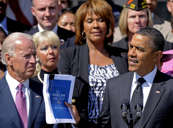 President Barack Obama, accompanied by Vice President Joe Biden, and others, holds up a copy of his American Jobs Act during a statement in the Rose Garden of the White House today.