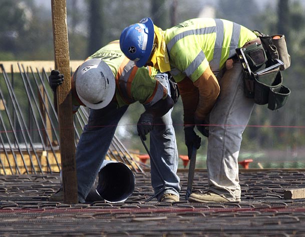 Construction workers check rebar on a highway construction project on Interstate 5 in Los Angeles Wednesday. The number of people seeking unemployment benefits fell sharply last week, an encouraging sign that layoffs are easing. The Associated Press