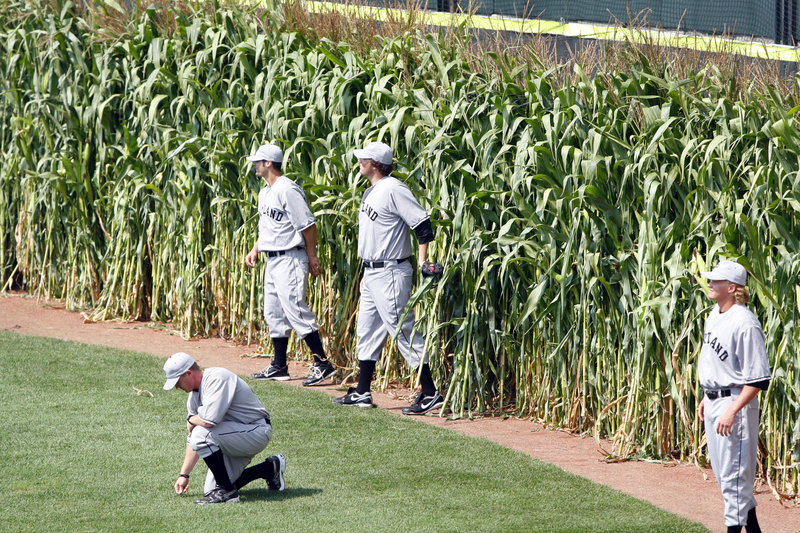 Portland Sea Dogs manager Kevin Boles kneels down to feel the grass of Hadlock Field as his players emerge from the corn in centerfield.