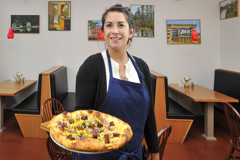 Server Marie Vella presents a specialty pizza, Cedric’s Pie, made with roasted onion and garlic, corn and local bison bacon on homemade dough, at Scarlet Begonias in Brunswick. The restaurant currently features the paintings of Lisbon artist Frank O. Gross Jr.