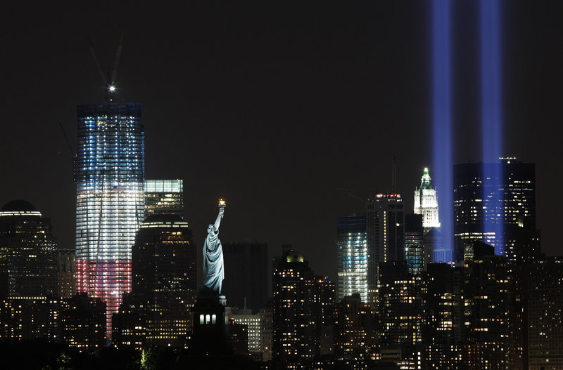 The Tribute in Light, visible at right, an art installation representative of the twin towers, shines above the altered lower Manhattan skyline that includes the Statue of Liberty and the new One World Trade Center, left.