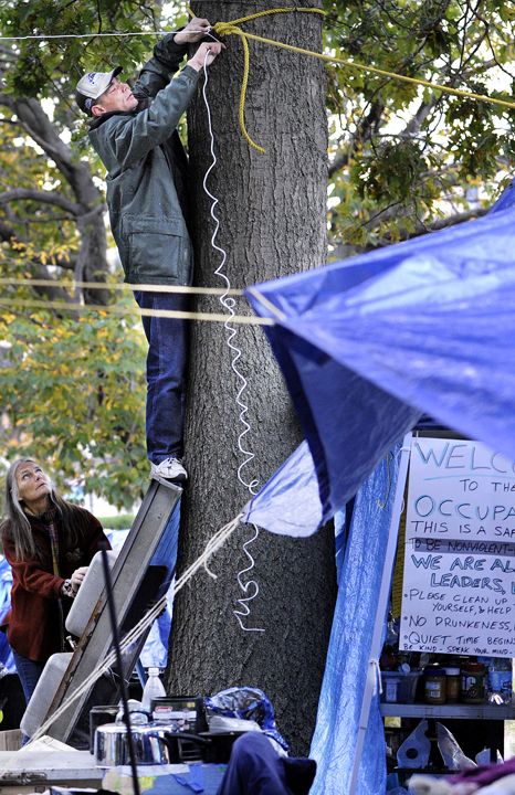 Alan Porter, 45, of Portland shimmied up a tree in Lincoln Park to secure a rope as part of a support system for a tarp to protect Occupy Maine's belongings against impending rain.