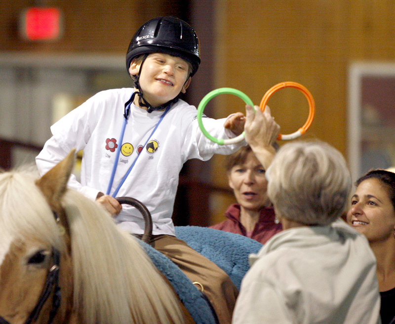 Sarah Bronson, executive director of the Riding to the Top Therapeutic Riding Center in Windham, holds up rings for Scotty Wentzell, 10, to grab as Diane Powers of the riding center, middle, and Scotty’s mother, Lisa Wentzell, encourage him.