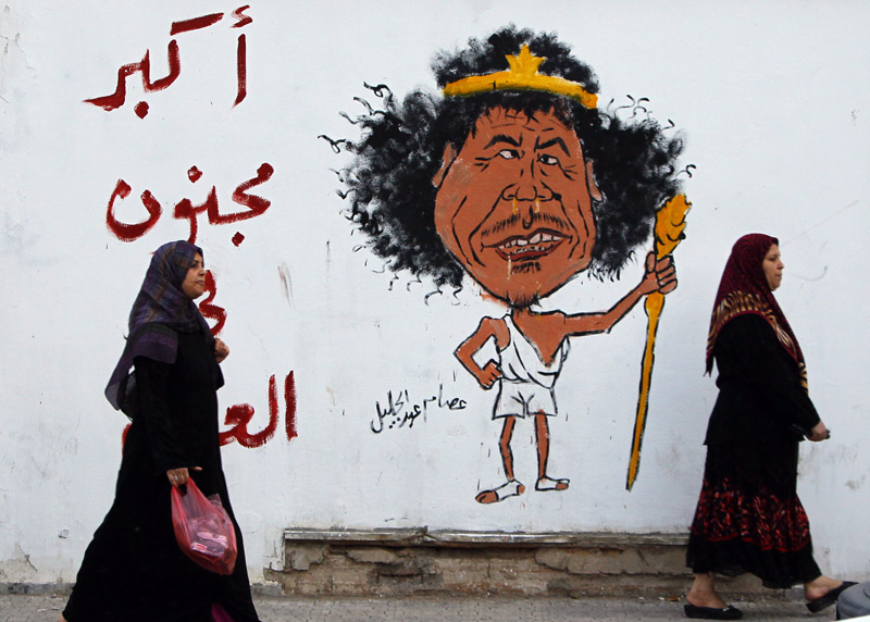 Libyan women walk past a graffiti reading: "The greatest Crazy of the World" in Tripoli, Libya. The death Thursday of Gadhafi, two months after he was driven from power and into hiding, decisively buries the nearly 42-year regime that had turned the oil-rich country into an international pariah and his own personal fiefdom.
