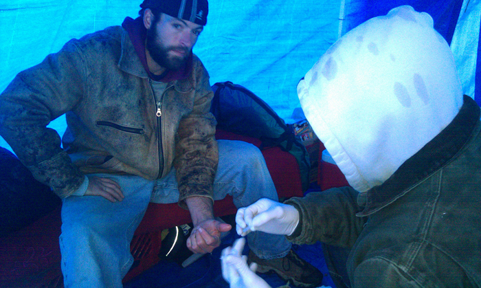 Christopher Makelys, who is in charge of medical care at the Occupy Maine encampment in Portland's Lincoln Park, treats a cut on the finger of fellow protester Larry Vanscyoc in the group's medical tent.