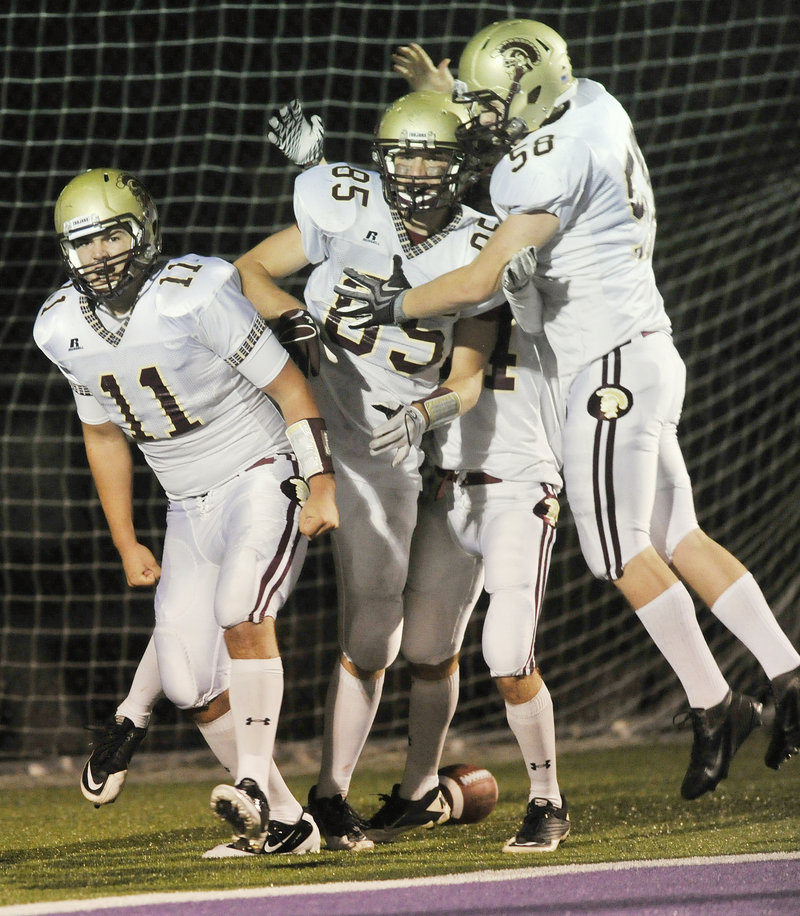 Thornton Academy quarterback Eric Christensen, left, is joined by teammates after scoring on an 8-yard run in the final minute of the first half Friday night. The Trojans went on to beat Deering.