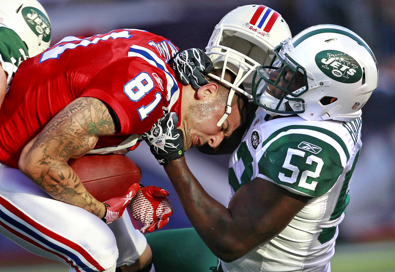Aaron Hernandez of the Patriots, left, holds onto the ball as David Harris of the Jets rips off his helmet on a hit in the first half Sunday in Foxborough, Mass.