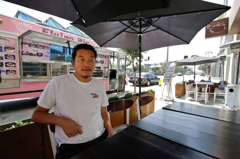 Owner Joe Kim sits at an outdoor table at the newly opened Flying Pig restaurant in Los Angeles, Calif. The Flying Pig started out as a food truck, visible at the rear, as a way for Kim to test out recipes before launching a restaurant.