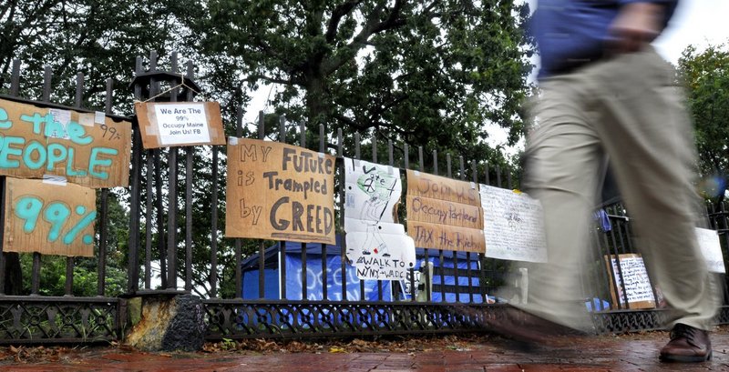A pedestrian on Oct. 4 walks past signs placed on the fence of Lincoln Park in Portland by the group Occupy Maine.
