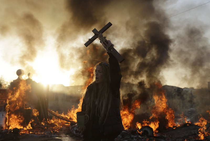 An Irish Traveler holds a cross in front of a burning barricade during Wednesday’s evictions.