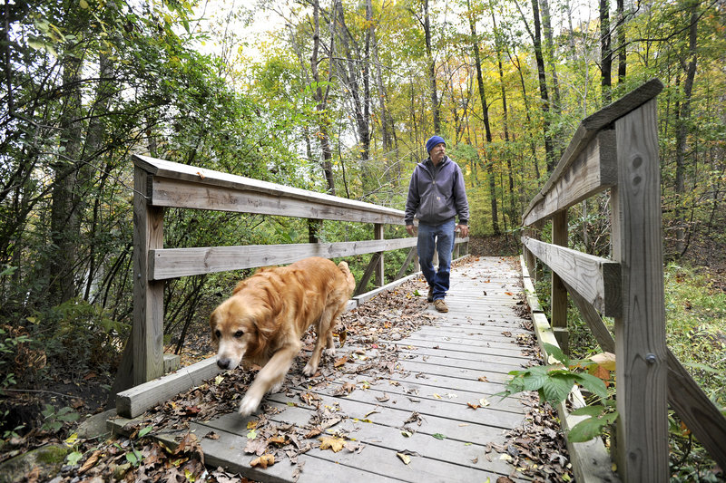Tim Hopkins of Portland and his dog Minie cross a bridge in a section of the Sebago to the Sea Trail in the Riverton Trolley Park in Portland. A new stretch of the trail, from South Windham to Falmouth, opens today.