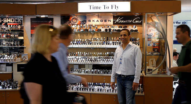 Ben Cohen, owner of “Time To Fly” in Philadelphia International Airport’s Terminal B, talks with passengers as they walk by his kiosk. For 16 years, Cohen has operated a cart at the airport selling watches priced from $25 to $900.