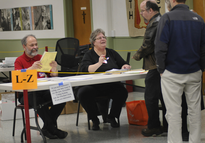 Tim Whitney and Susan Garfield of Portland, election clerks at St. Pius Church polling place in Portland, check in voters today.