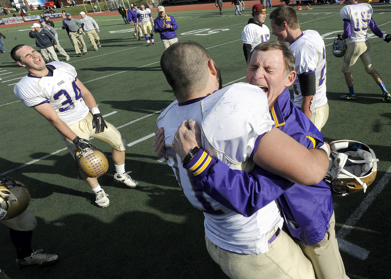 Cheverus Coach John Wolfgram hugs team co-captain Christian Deschenes as teammate Coleman Walsh (34) celebrates after Cheverus defeated Lawrence 49-7 for its second straight Class A state football championship at Fitzpatrick Stadium in Portland Saturday. The win also marked the 10th state title of Wolfgram’s illustrious career.