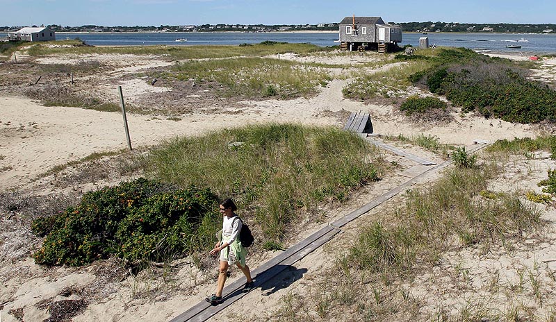 In this Aug. 23, 2011, photo, Susan Carroll, an occupant of one of the 11 cottages on North Beach Island in Chatham, Mass., walks from the beach to her cottage. On Tuesday, the Keeper of the National Register of Historic Places denied protection for five of the cottages slated to be torn down, saying they aren't rare or historically important enough to qualify for the list. The decision means their owner, the federal Cape Cod National Seashore, can proceed with demolition.