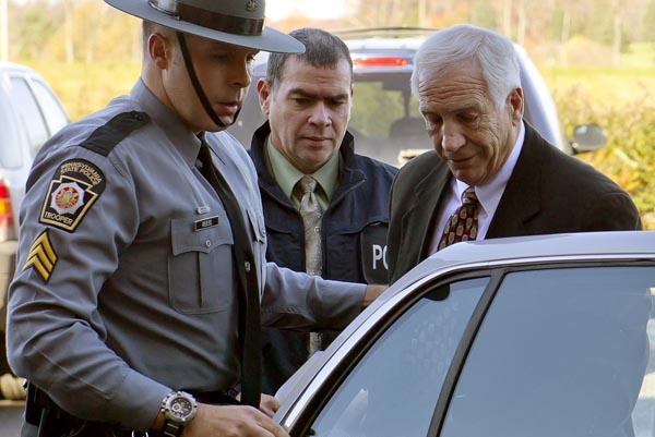 Former Penn State football defensive coordinator Gerald "Jerry" Sandusky, center, arrives in handcuffs at the office of Centre County Magisterial District Judge Leslie A. Dutchcot while being escorted by Pennsylvania State Police and Attorney General's Office officials on Saturday, Nov. 5, in State College, Pa.