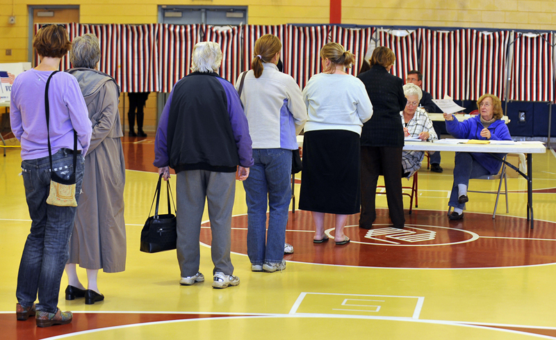 Hana Strnad, right, election clerk at the Boys and Girls Club voting place in South Portland, hands a ballot to a voter while fellow election clerk Linden Thigpen, to Strnad's left, verifies the each voter's eligibility.