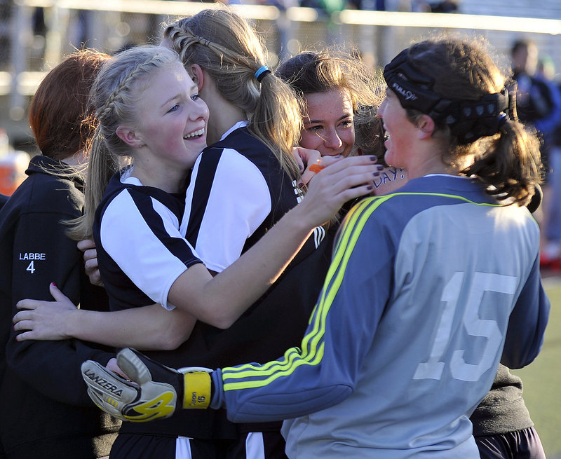 Kayla McLellan, left, is hugged by teammates, including goalkeeper Mary Caron, right, after helping set up the overtime goal by Dayle Jordan that gave St. Dominic of Auburn a 1-0 victory against Waynflete in the Western Class C girls’ soccer final Wednesday at Fitzpatrick Stadium.