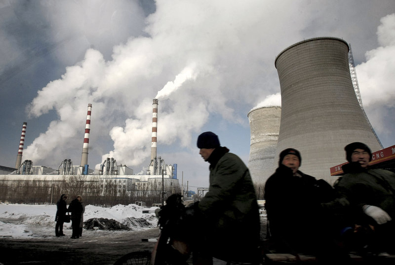 Workers pass a coal-fired power plant on a tricycle cart in Changchun, in northeast China’s Jilin province last year. The world’s emissions of heat-trapping carbon dioxide took the biggest jump on record in 2010, the U.S. Department of Energy calculated.
