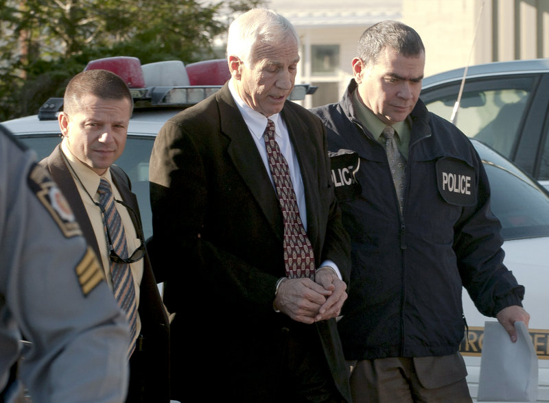 Jerry Sandusky, center, former defensive coordinator for the Penn State football team, is escorted to a police car Saturday in Bellefonte, Pa. He is charged with sexually abusing eight boys.