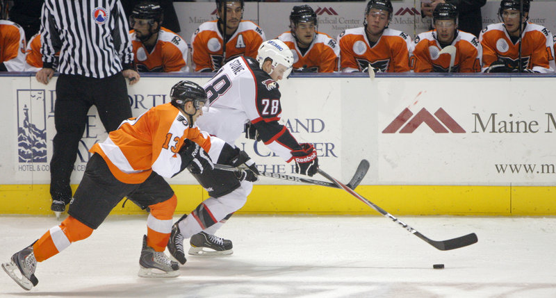 Michael Stone of the Portland Pirates brings the puck in front of the Philadelphia bench as Garrett Roe of the Phantoms gives chase.