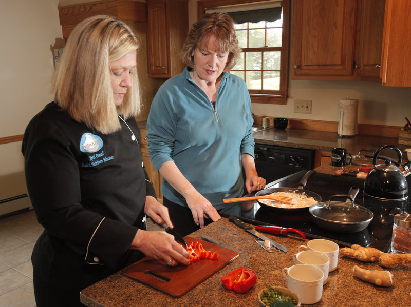 April Powell, left, teaches Marcia Scott how to make simple ginger curry chicken at Scott’s home in Arundel. Powell runs a company called InviteAbitE, which helps clients shop for and cook with nutrient-dense whole foods. Scott competes in triathlons and was looking for meals that would work well with her training.